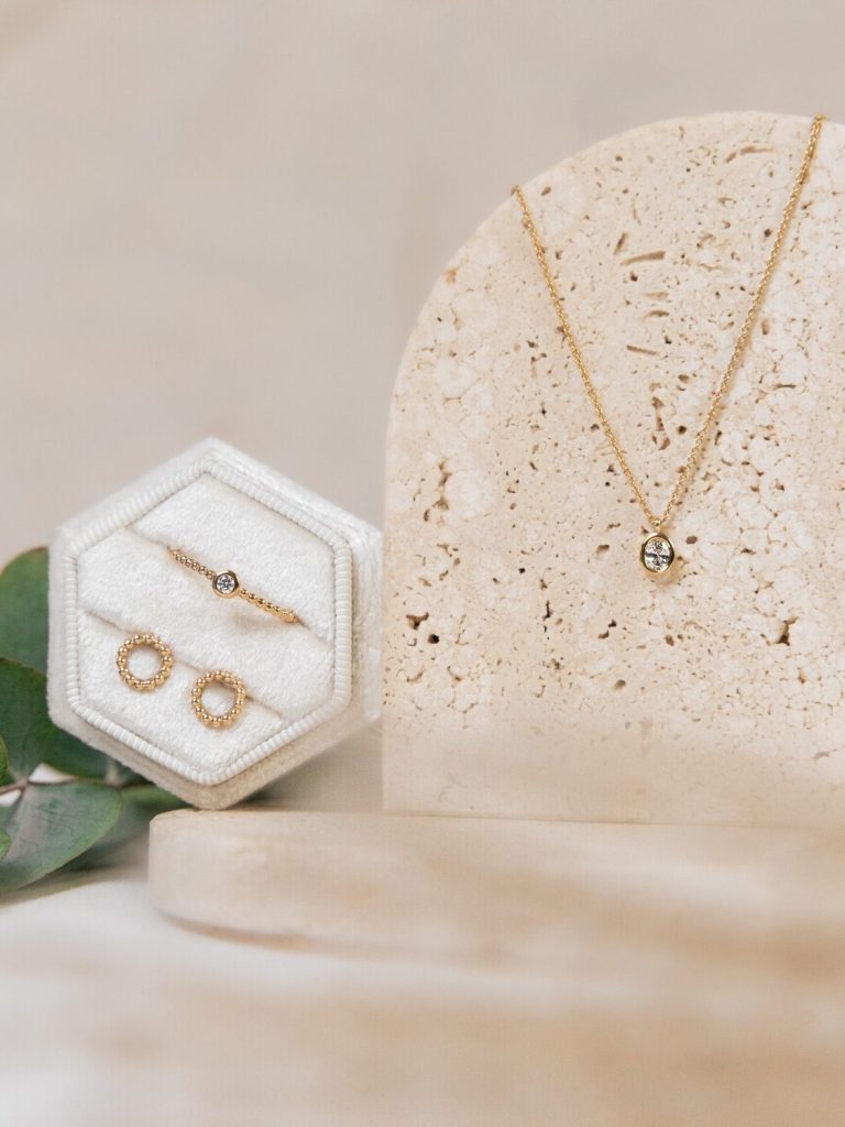 Schmuckstück mit goldener Halskette und Ohrringen auf natürlichem Untergrund.